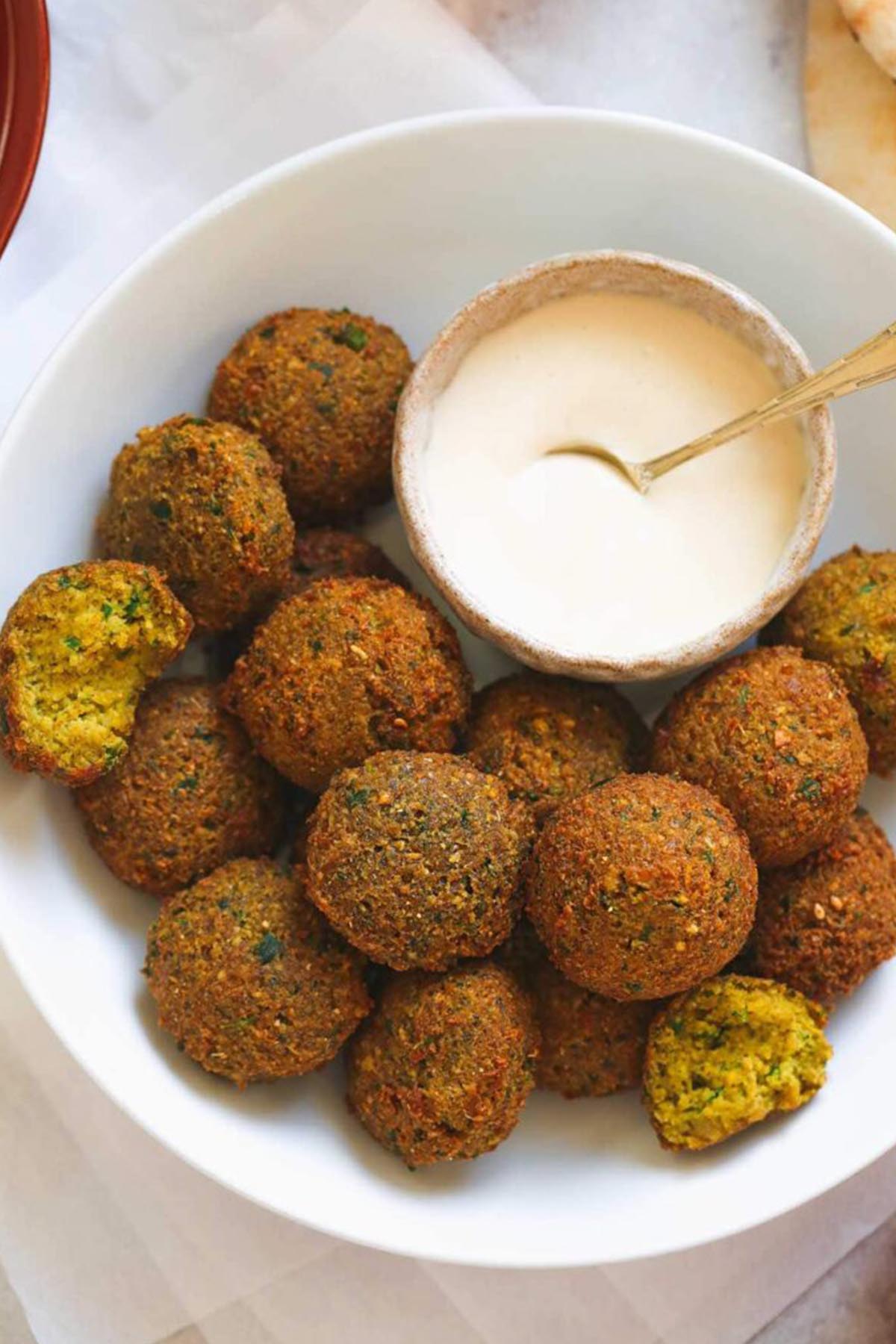 falafel balls in a bowl next to dipping sauce.