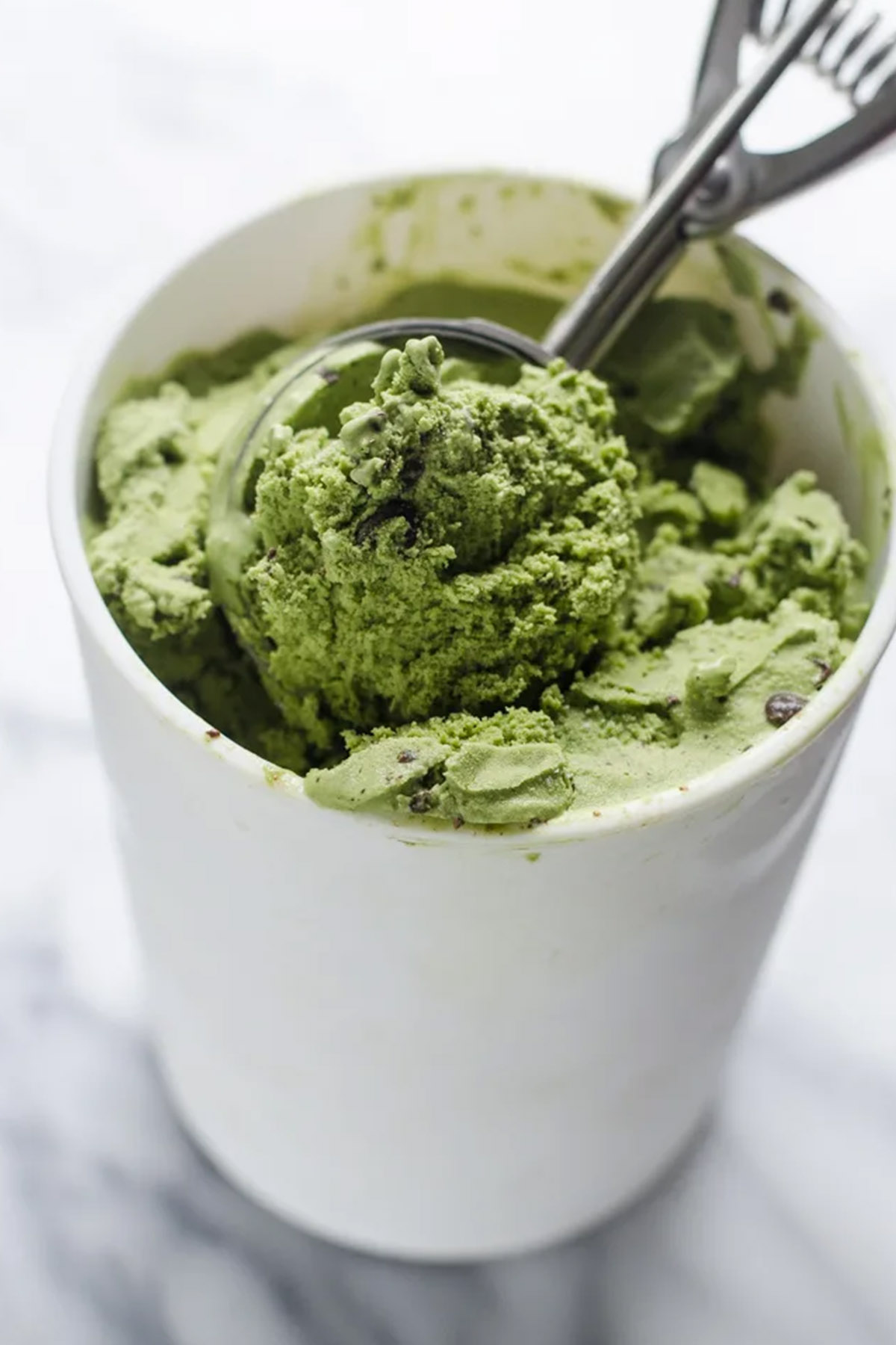 green ice cream in a pint container with an ice cream scoop.