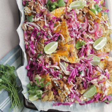 platter of nachos topped with slaw and lime wedges.