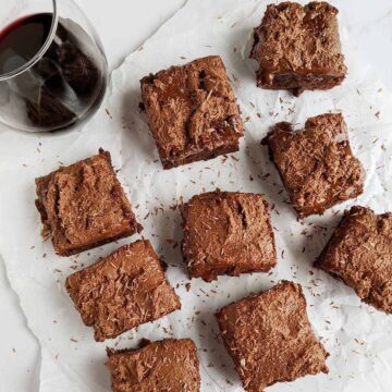 chocolate iced brownie slices on parchment paper next to a glass of wine.