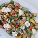 spinach salad topped with peach, burrata cheese, and tomatoes.