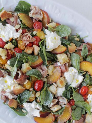 spinach salad topped with peach, burrata cheese, and tomatoes.