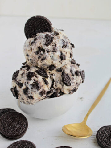 oreo cookie ice cream in a small serving bowl next to gold spoon.