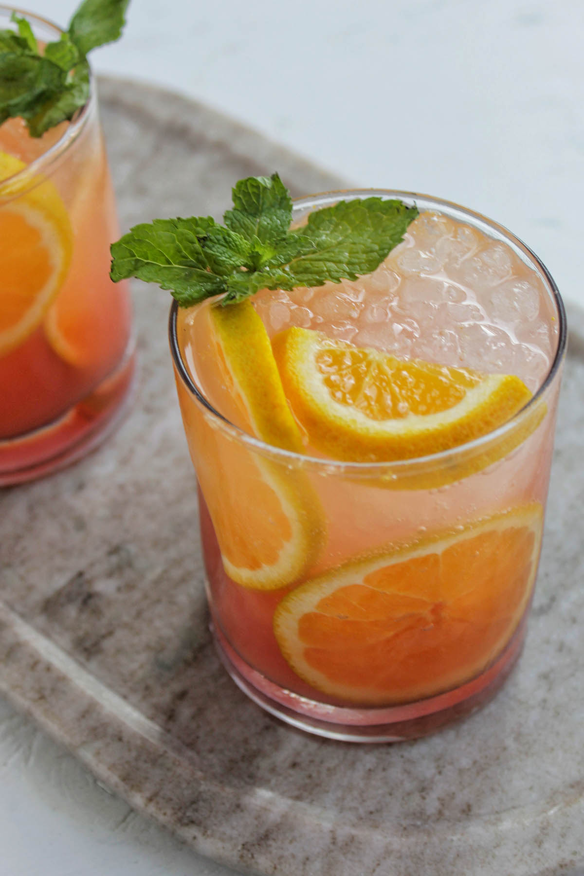 lowball glasses filled with and orange flavored cocktail and garnished with mint.