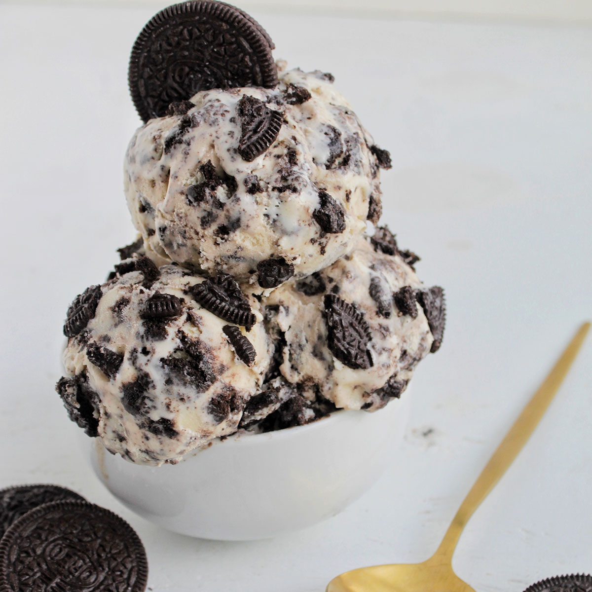 oreo cookie ice cream in a small serving bowl next to gold spoon.