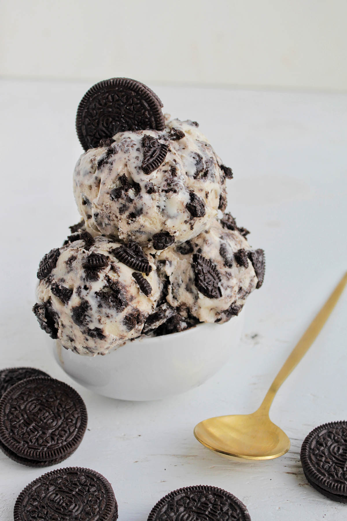 oreo cookie ice cream in a small serving bowl next to gold spoon.