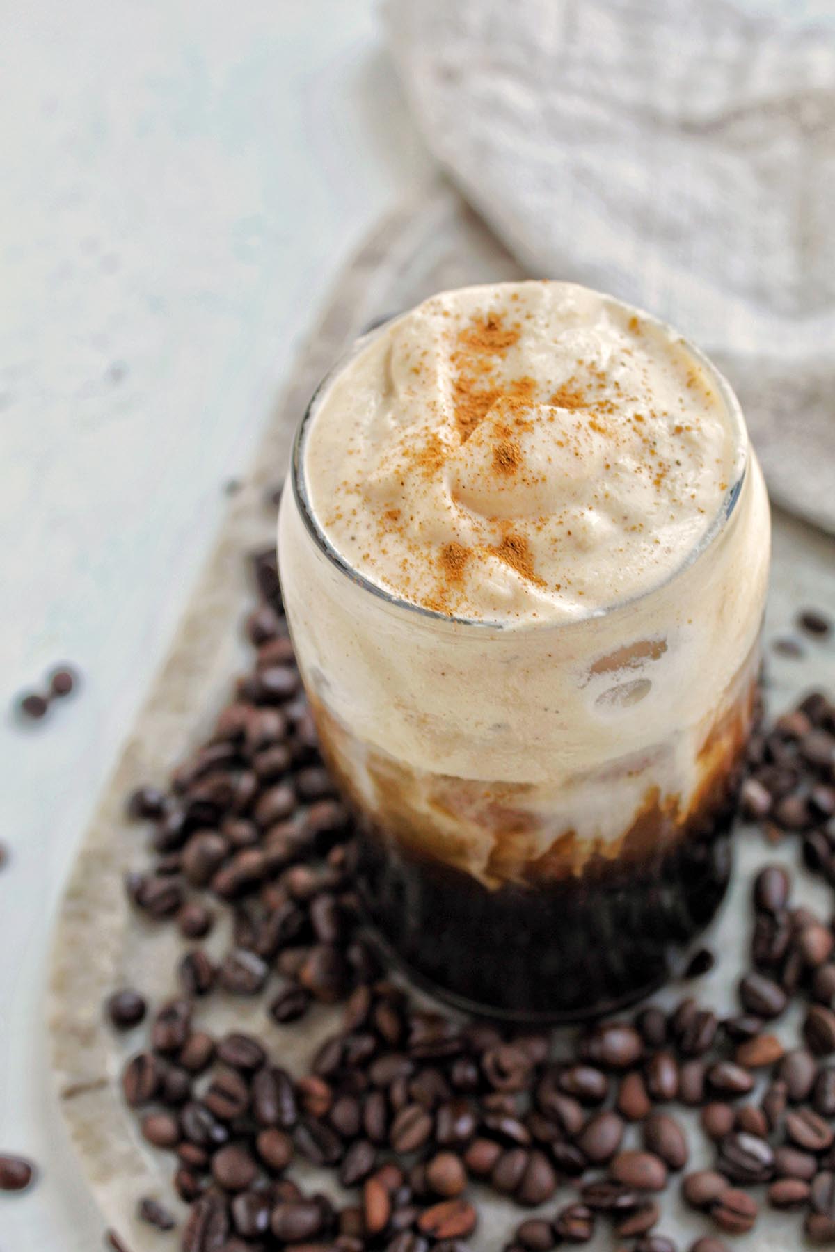 pumpkin cream cold brew in a glass next to coffee beans.