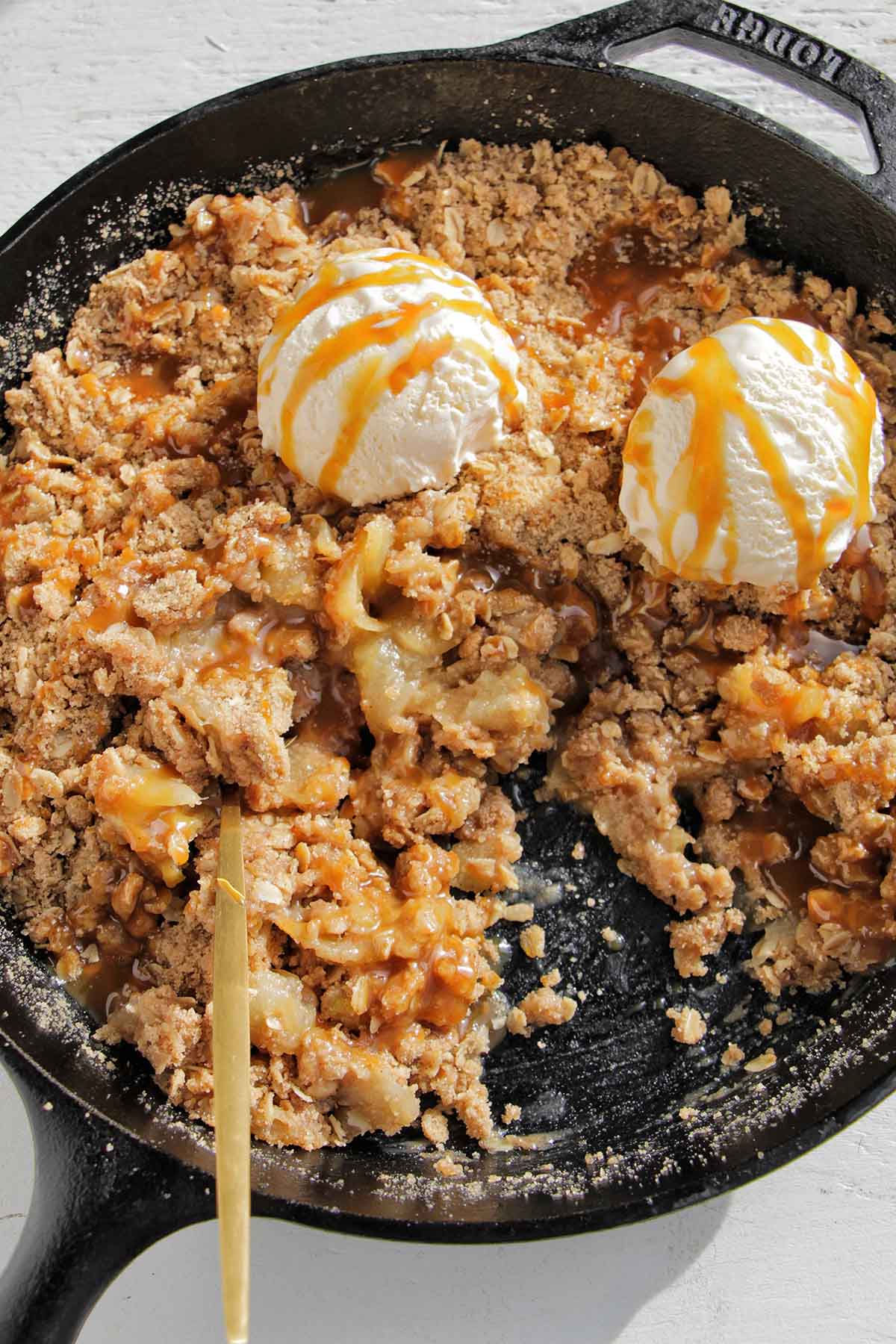 apple crisp topped with caramel and vanilla ice cream scoops.