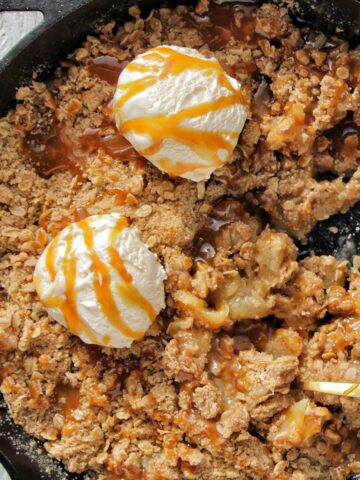 apple crisp in a cast iron skillet topped with ice cream scoops.