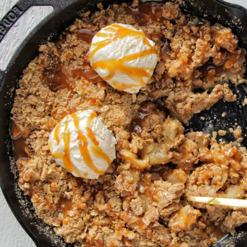 apple crisp in a cast iron skillet topped with ice cream scoops.