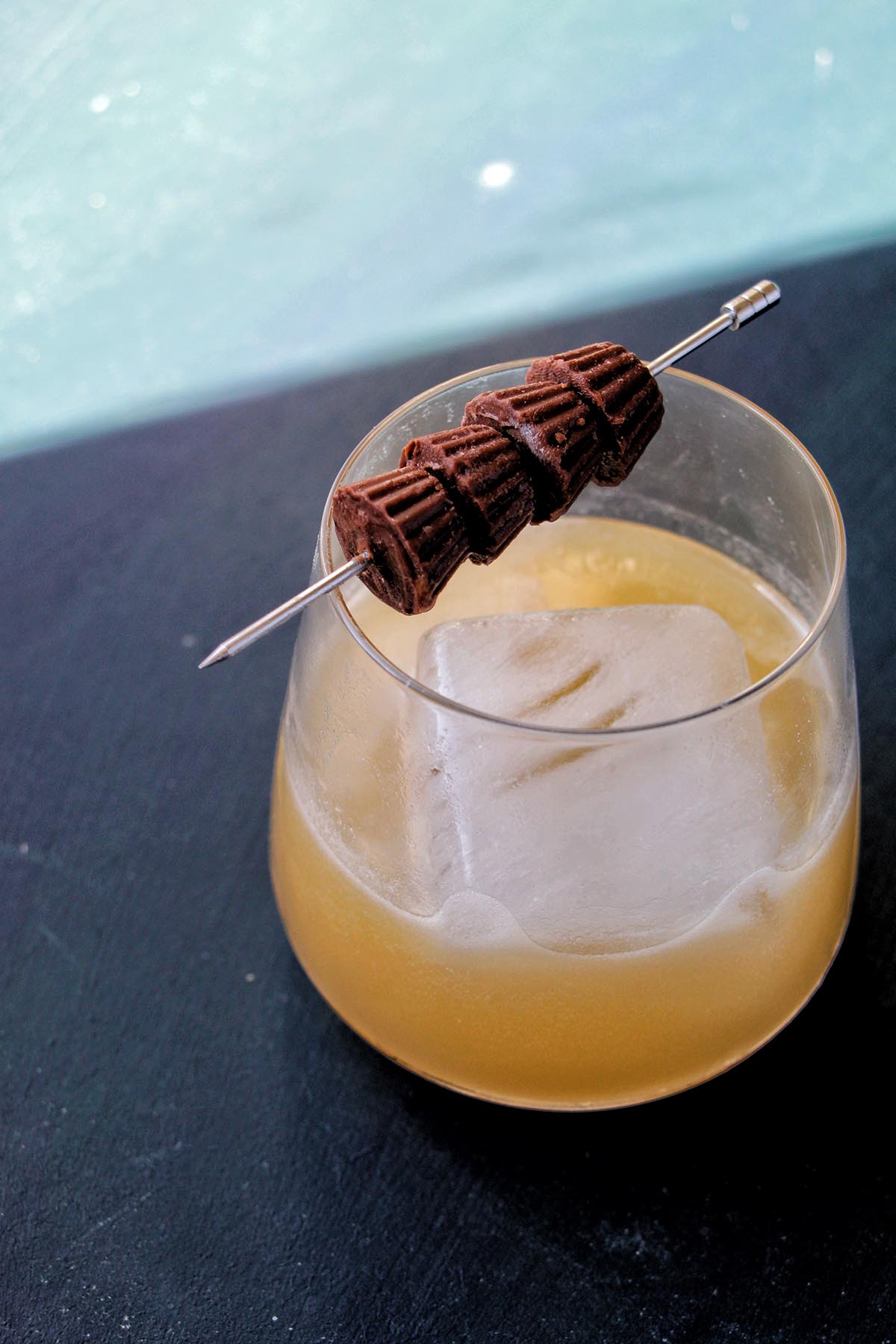 cocktail in a rocks glass with a large ice cube and peanut butter cup garnish.