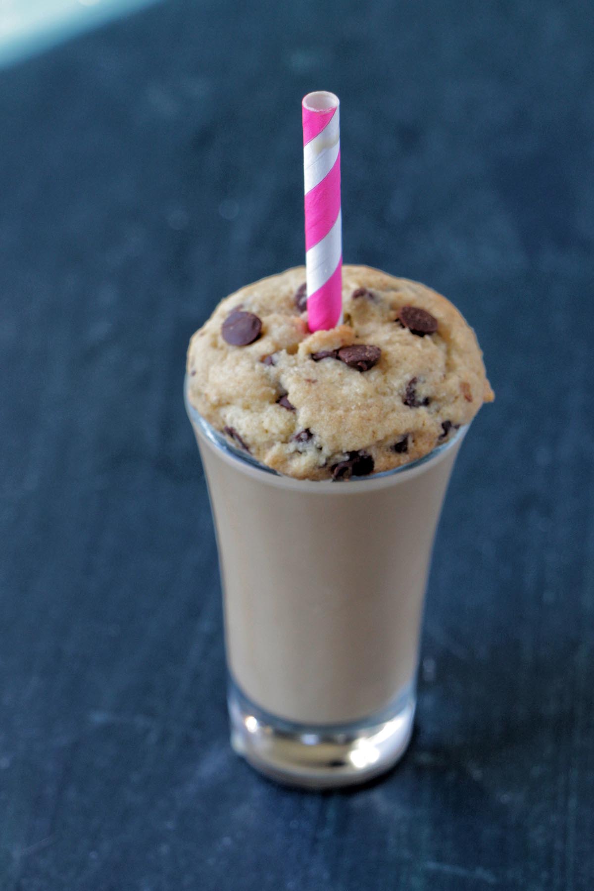 shot glass topped with a chocolate chip cookie and straw.