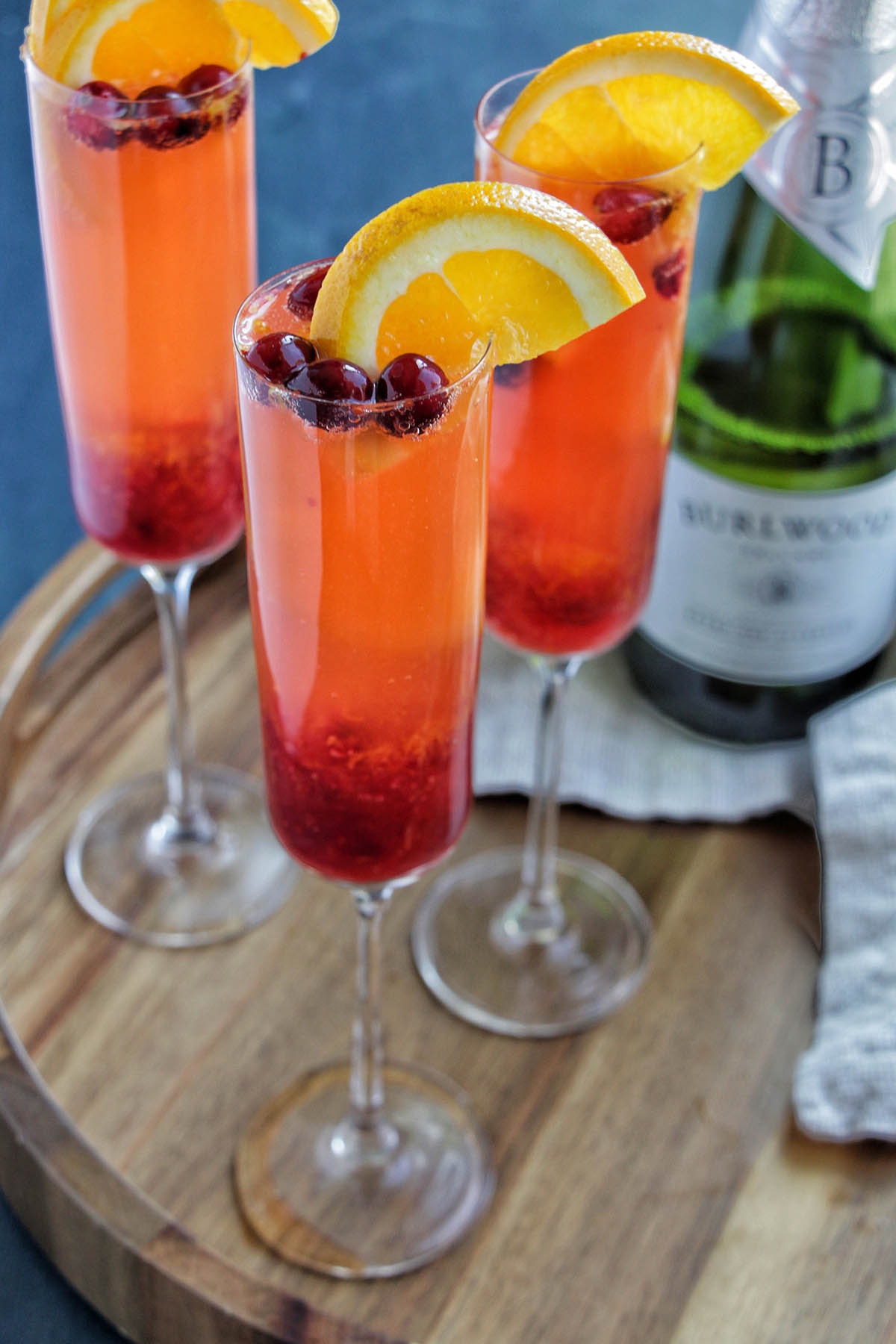 three champagne flutes garnishes with orange and cranberries.