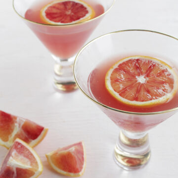 two pink martinis with blood orange slices on top.