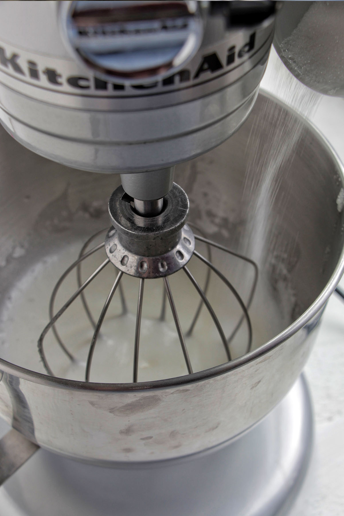 pouring sugar into a stand mixer with egg whites.