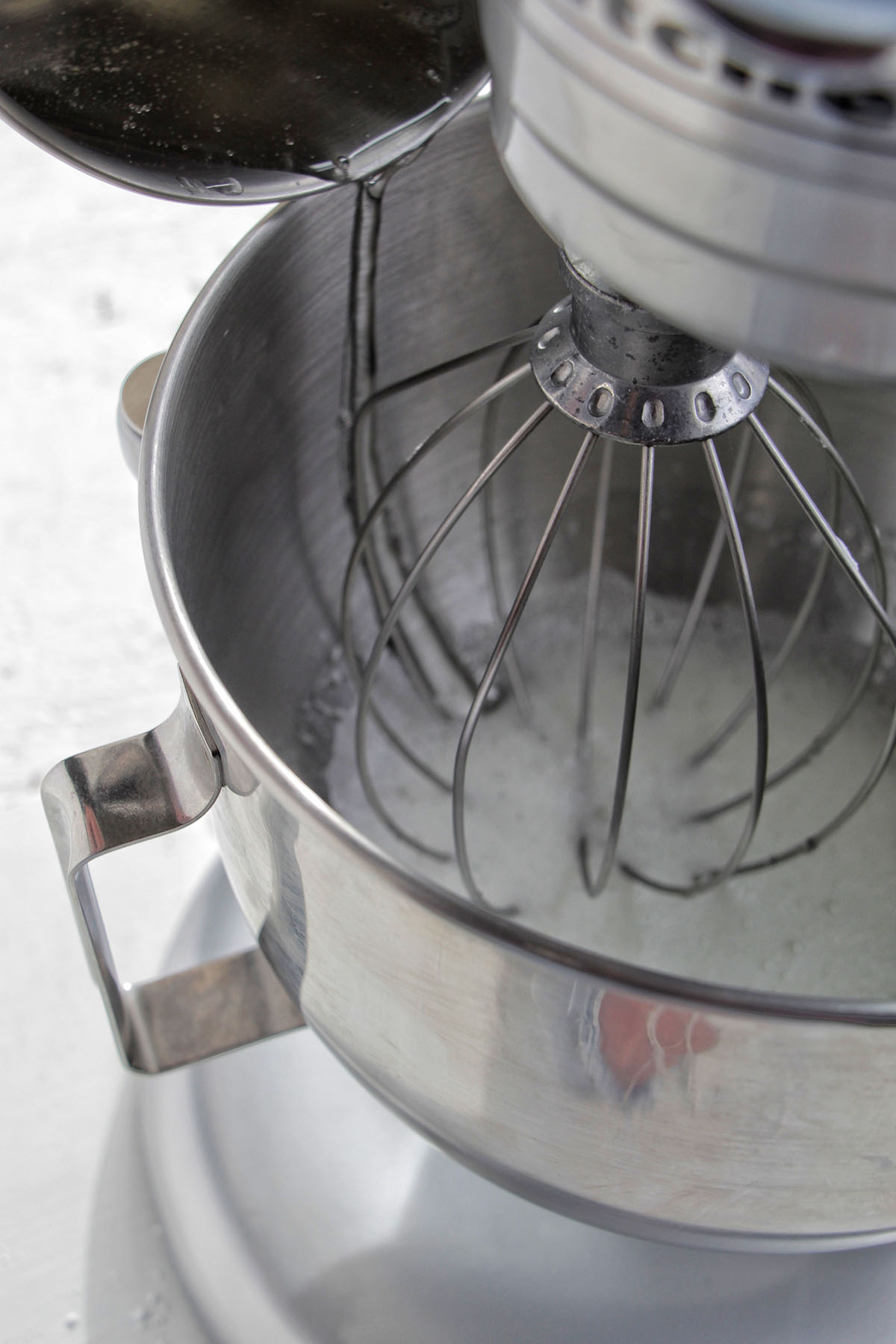 pouring liquid sugar into a stand mixer with egg whites.