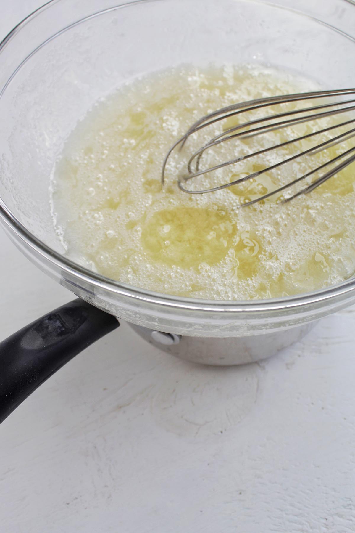 egg whites in a glass bowl sitting on top of a pot.