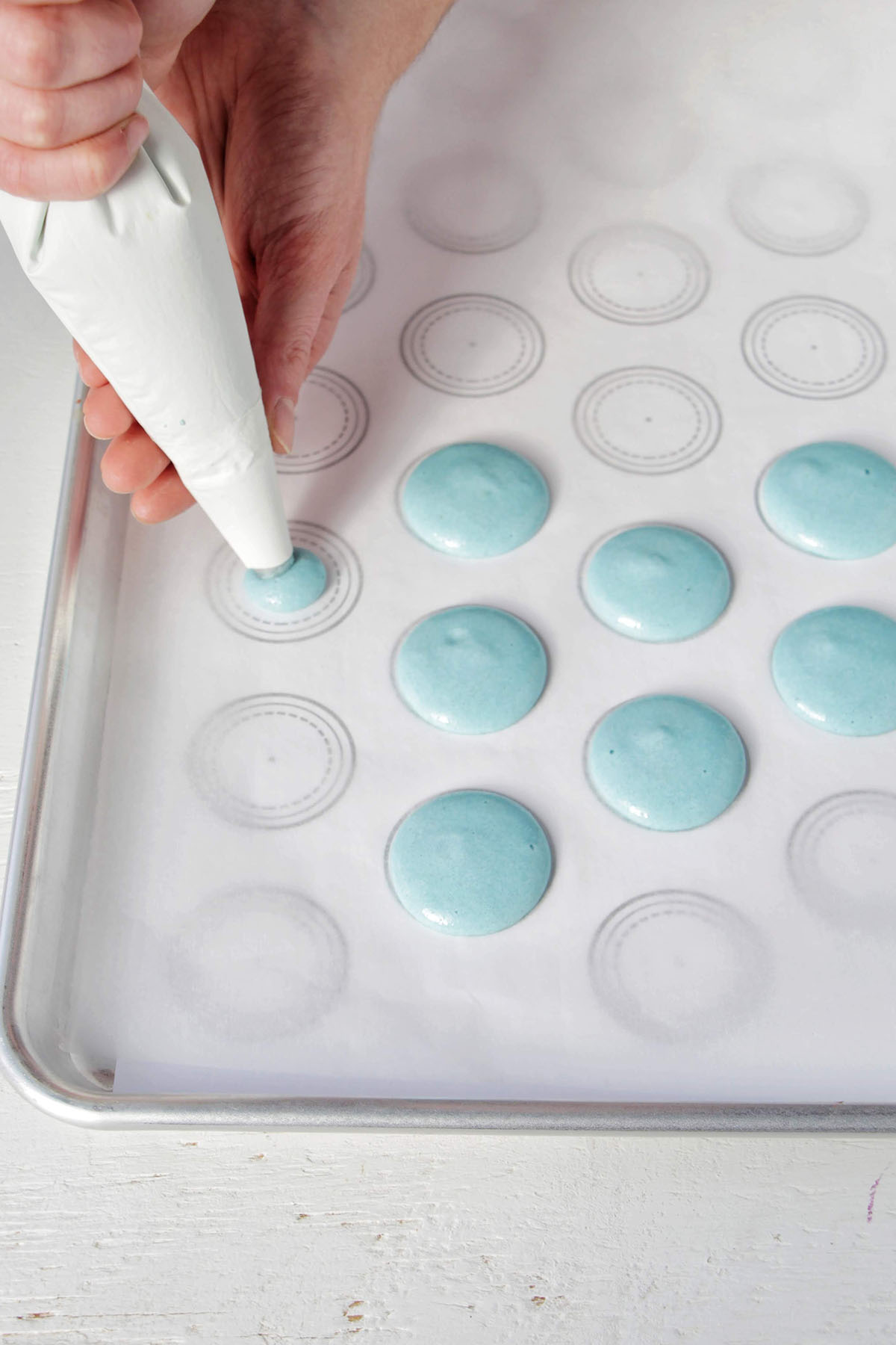 hand piping blue macarons on a parchment lined baking sheet.