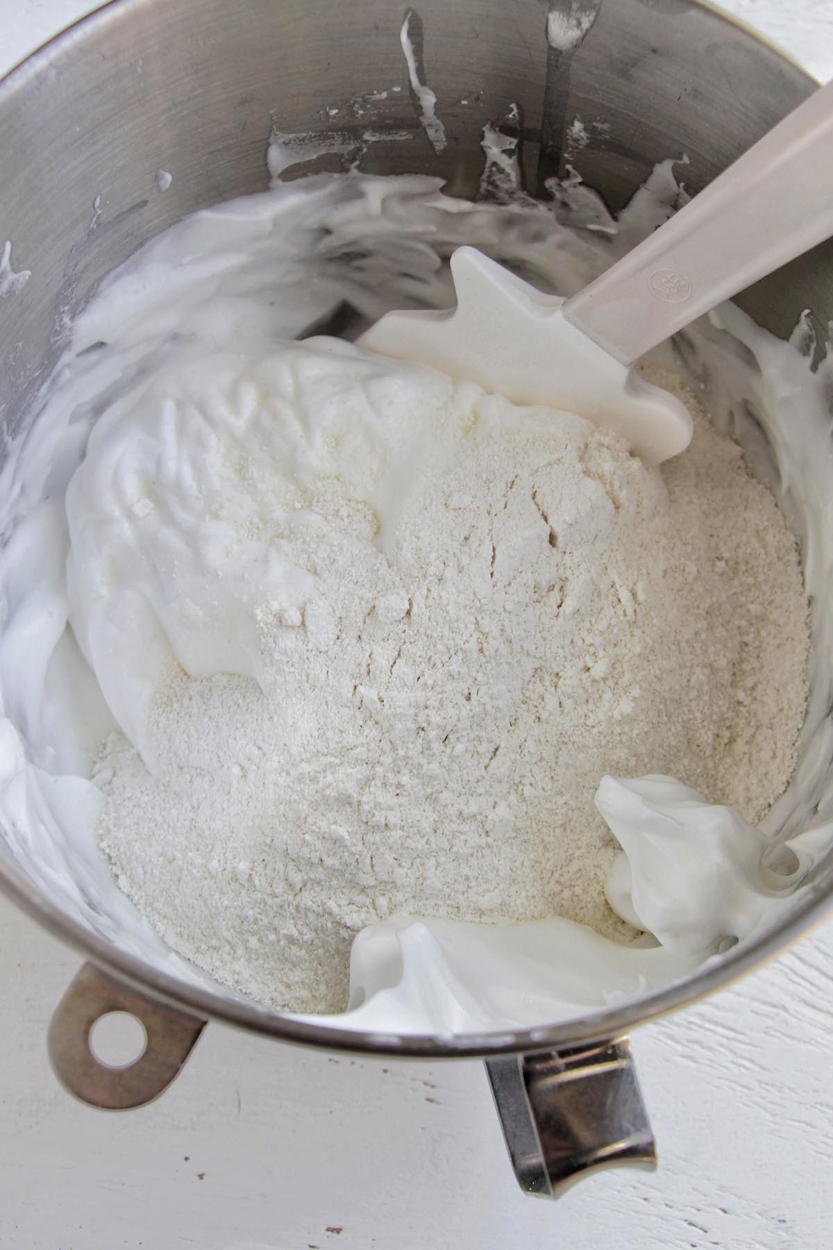 stiff peak meringue and almond flour in a mixing bowl with a silicone spatula.