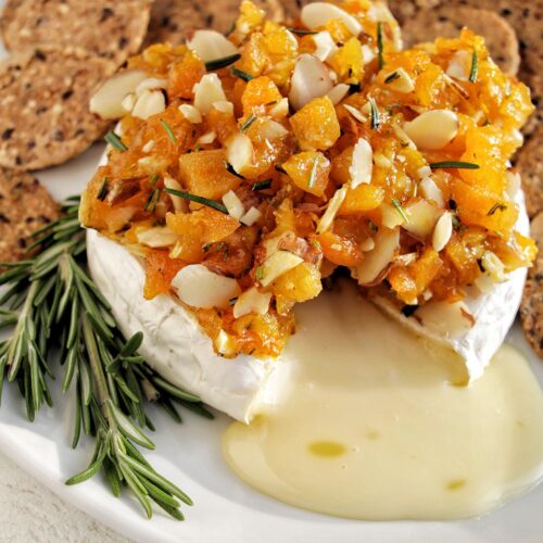 melted brie cheese topped with apricots on a serving tray with crackers.