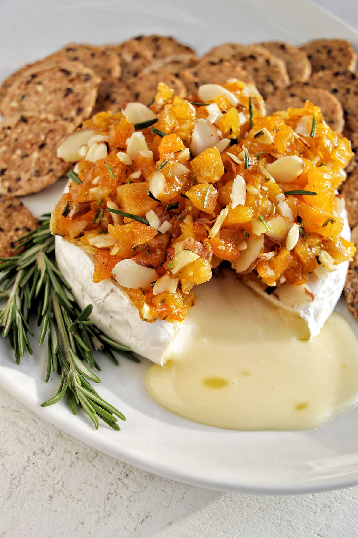 melted brie cheese topped with apricots on a serving tray with crackers.
