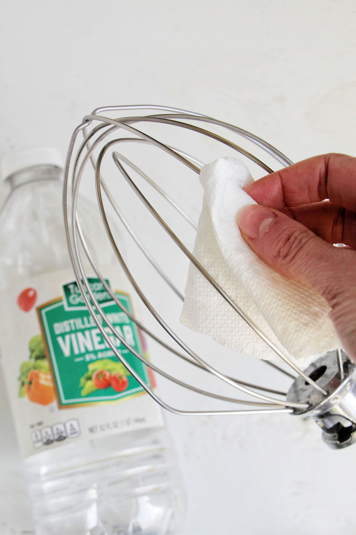 hand cleaning a whisk mixer attachment with a paper towel.