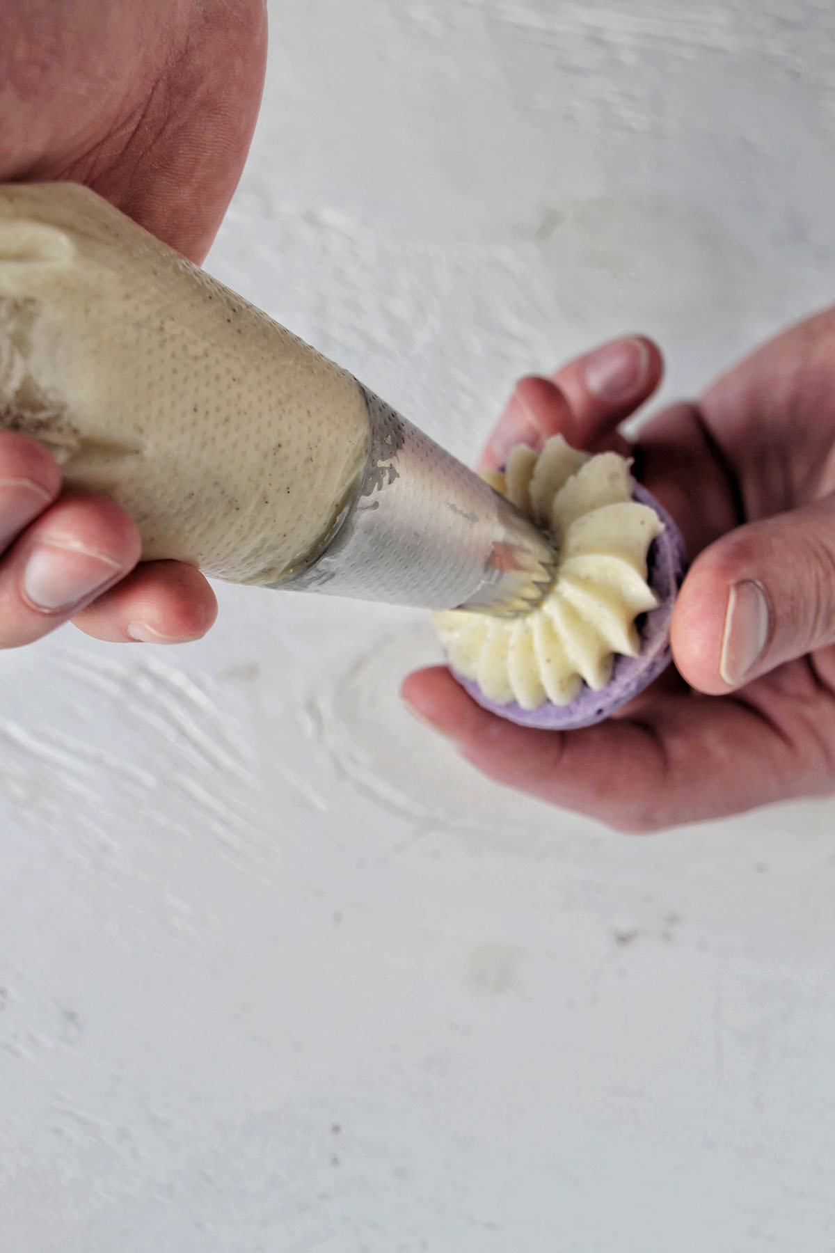 hand piping buttercream onto a purple macaron shell.