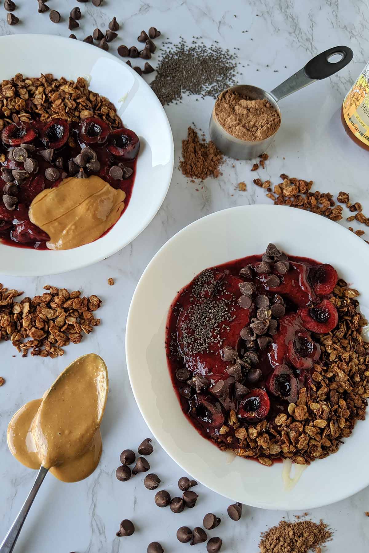 cherry chocolate granola smoothie bowl next to spoon with peanut butter.
