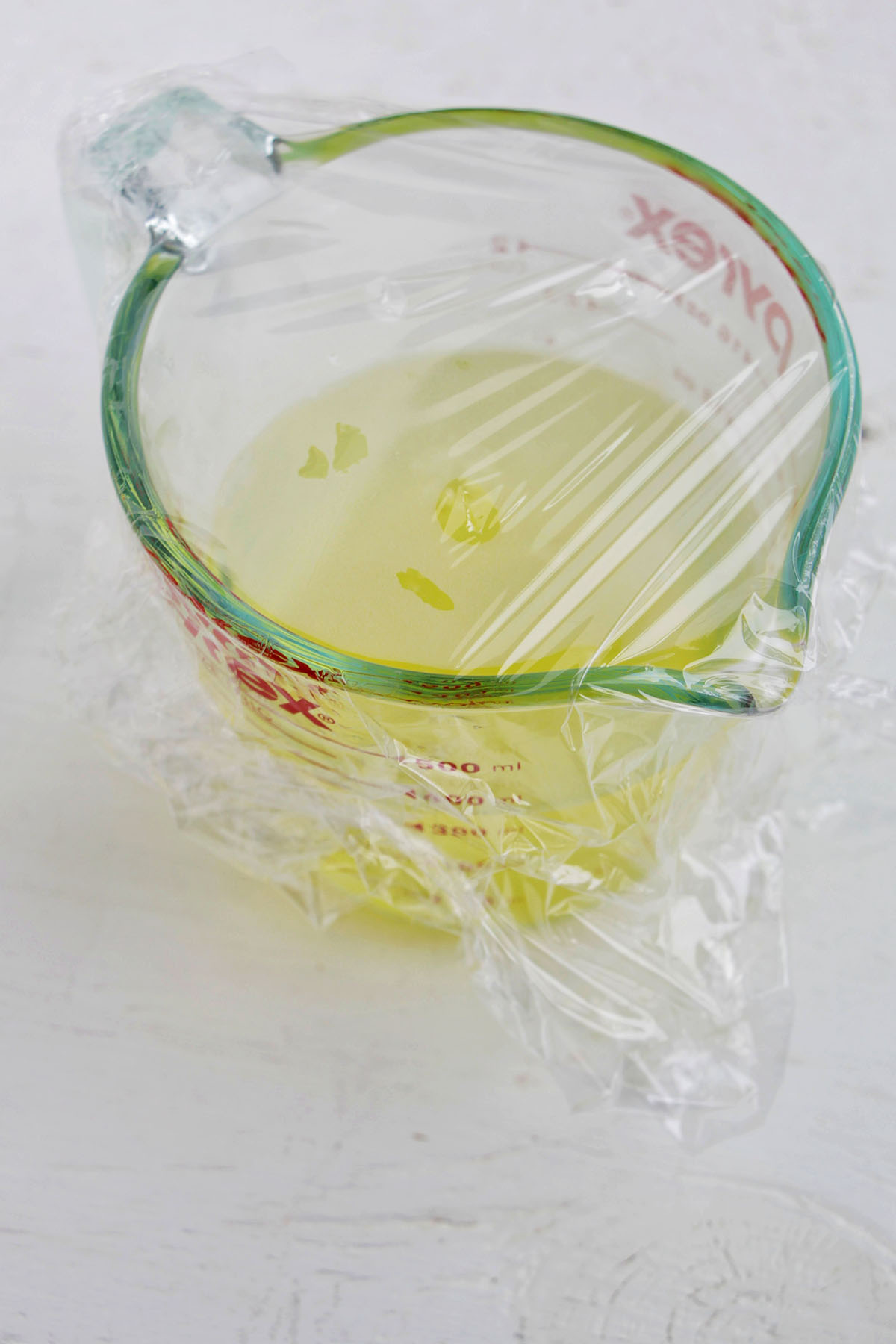 Pyrex glass measuring cup filled with egg whites and covered in plastic wrap.