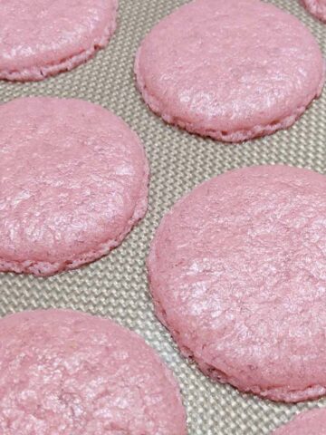 flattened pink macaron shells on a silicone mat.