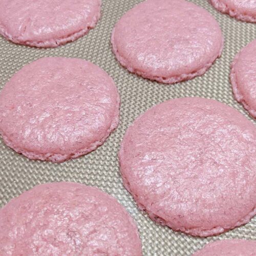 flattened pink macaron shells on a silicone mat.