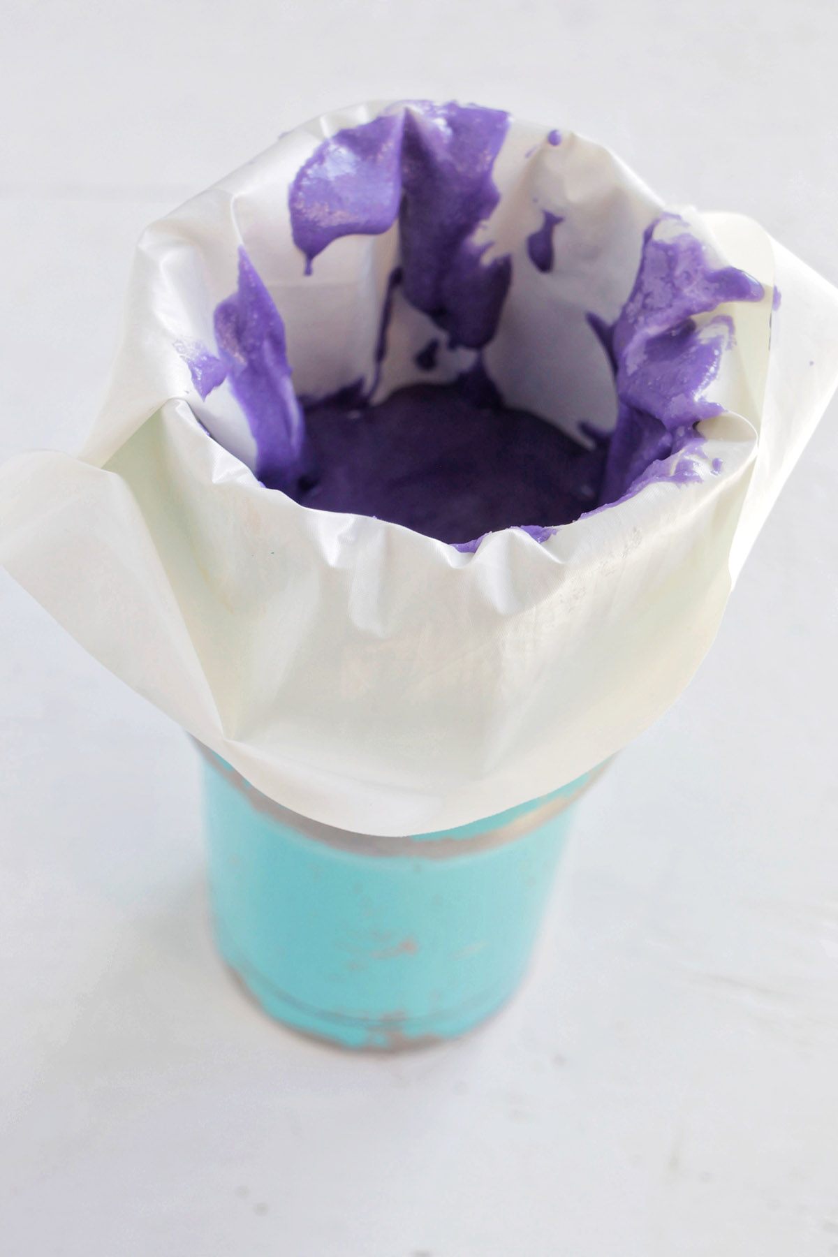 tall blue glass holding a piping bag filled with purple macaron batter.
