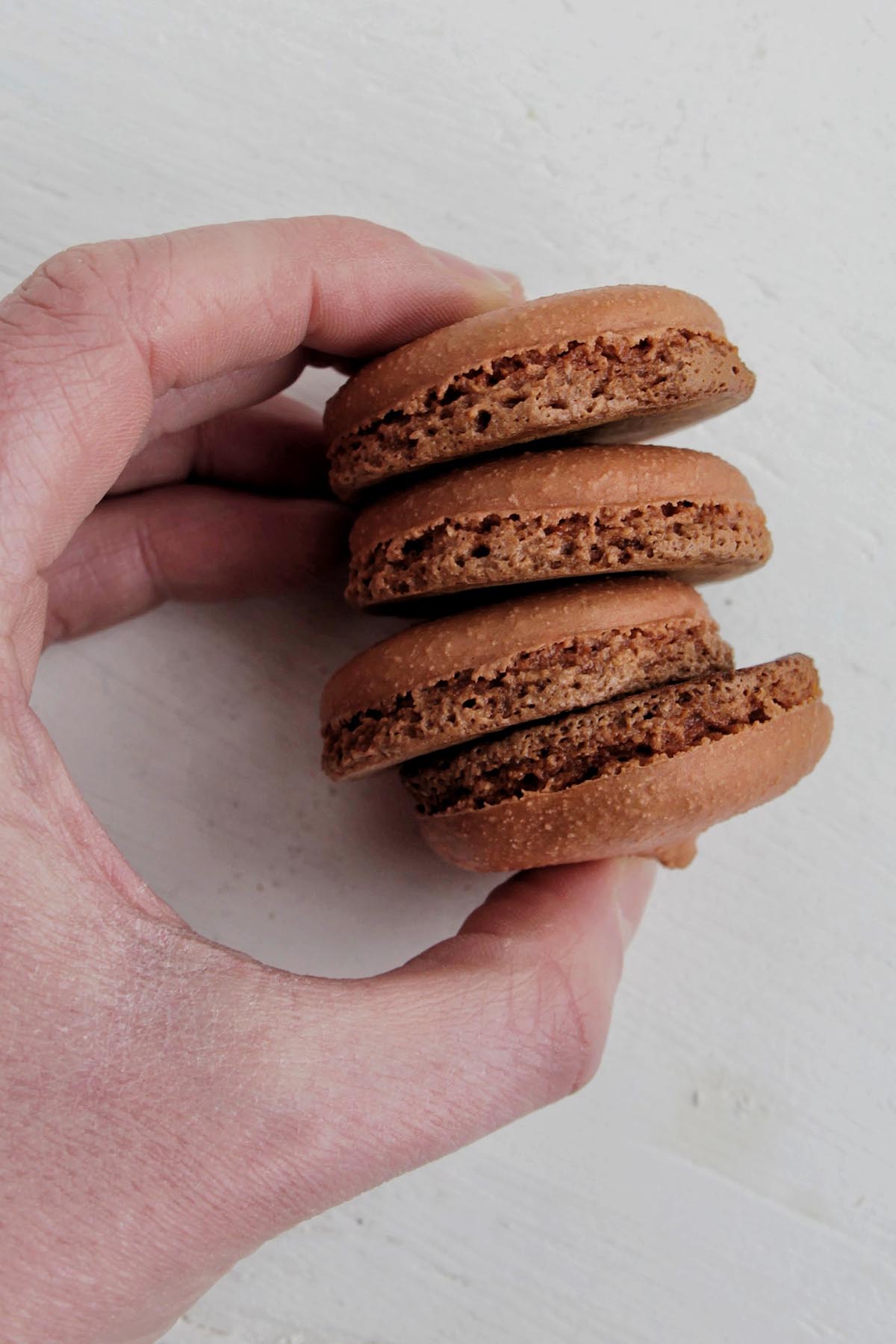hand holding four brown macaron shells with tall feet.