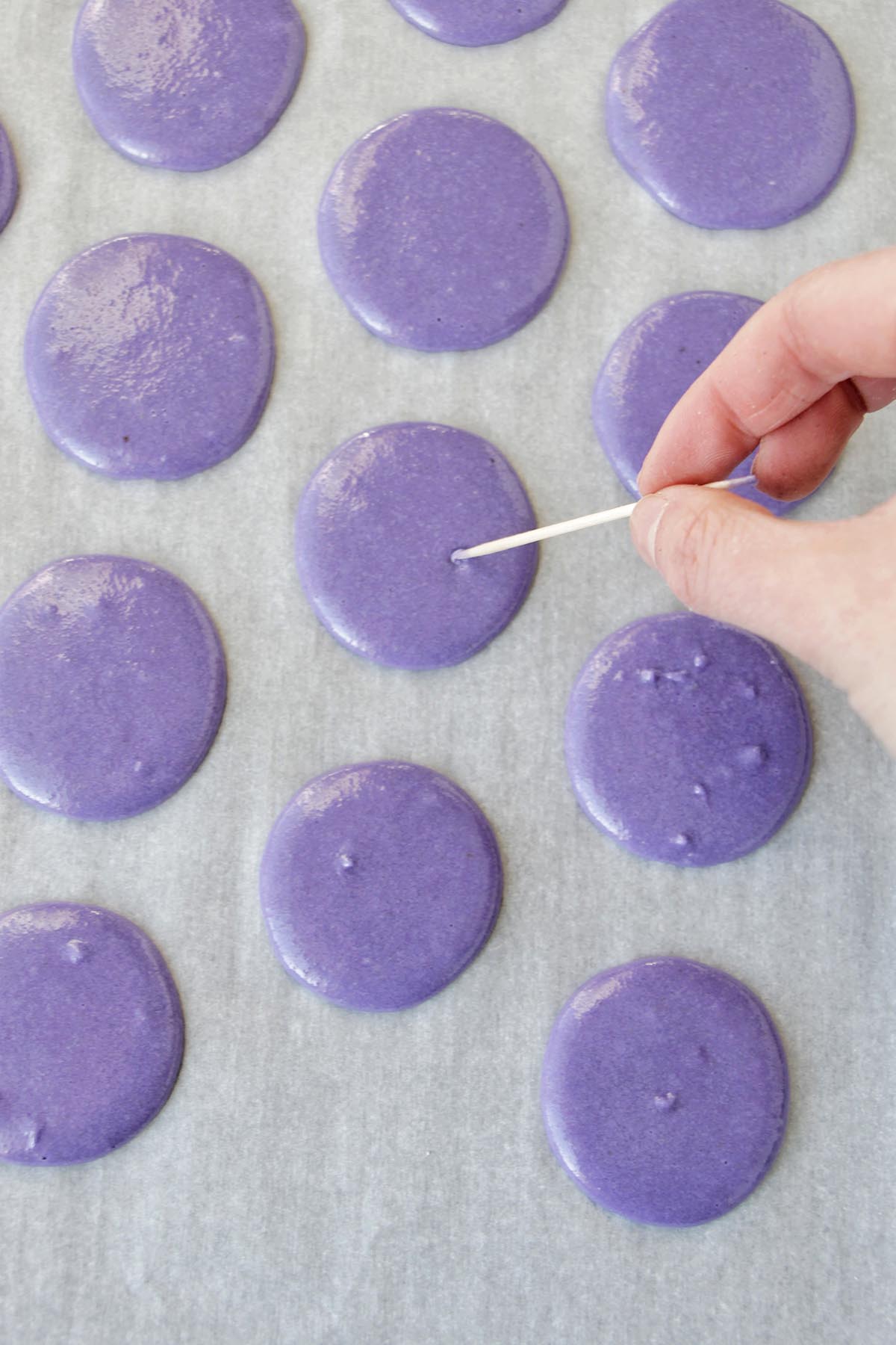popping air bubbles in macaron with a toothpick.