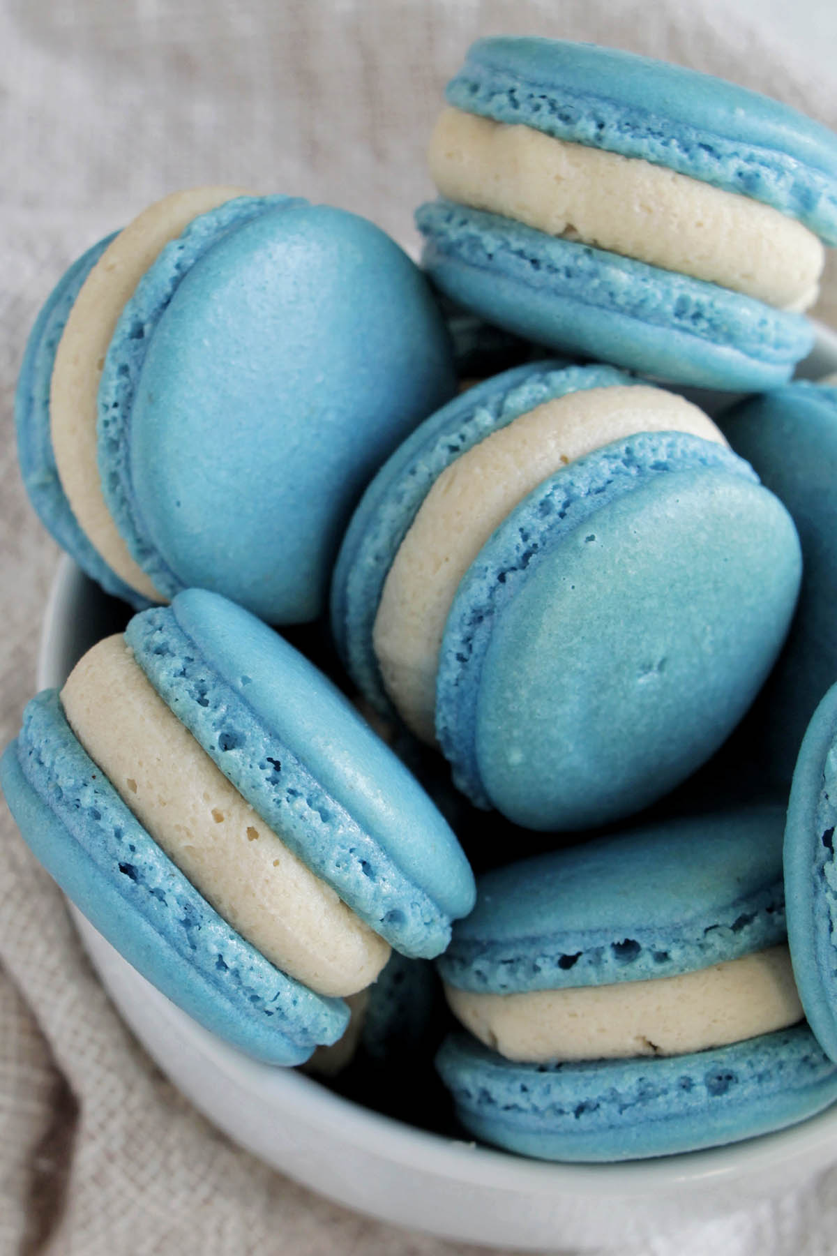 bowl filled with blue macarons filled with buttercream frosting.