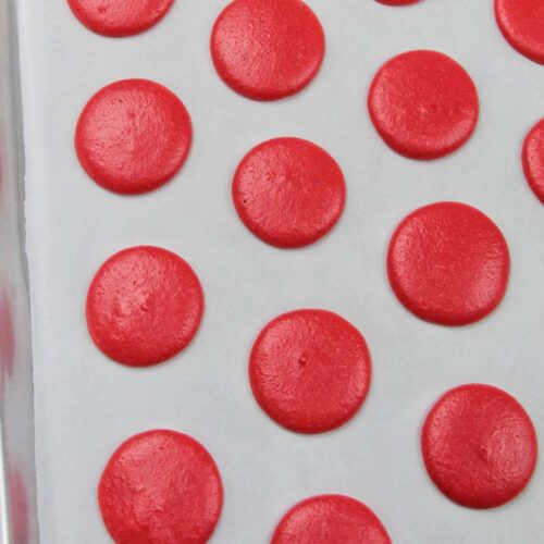red macaron shells drying on parchment paper.