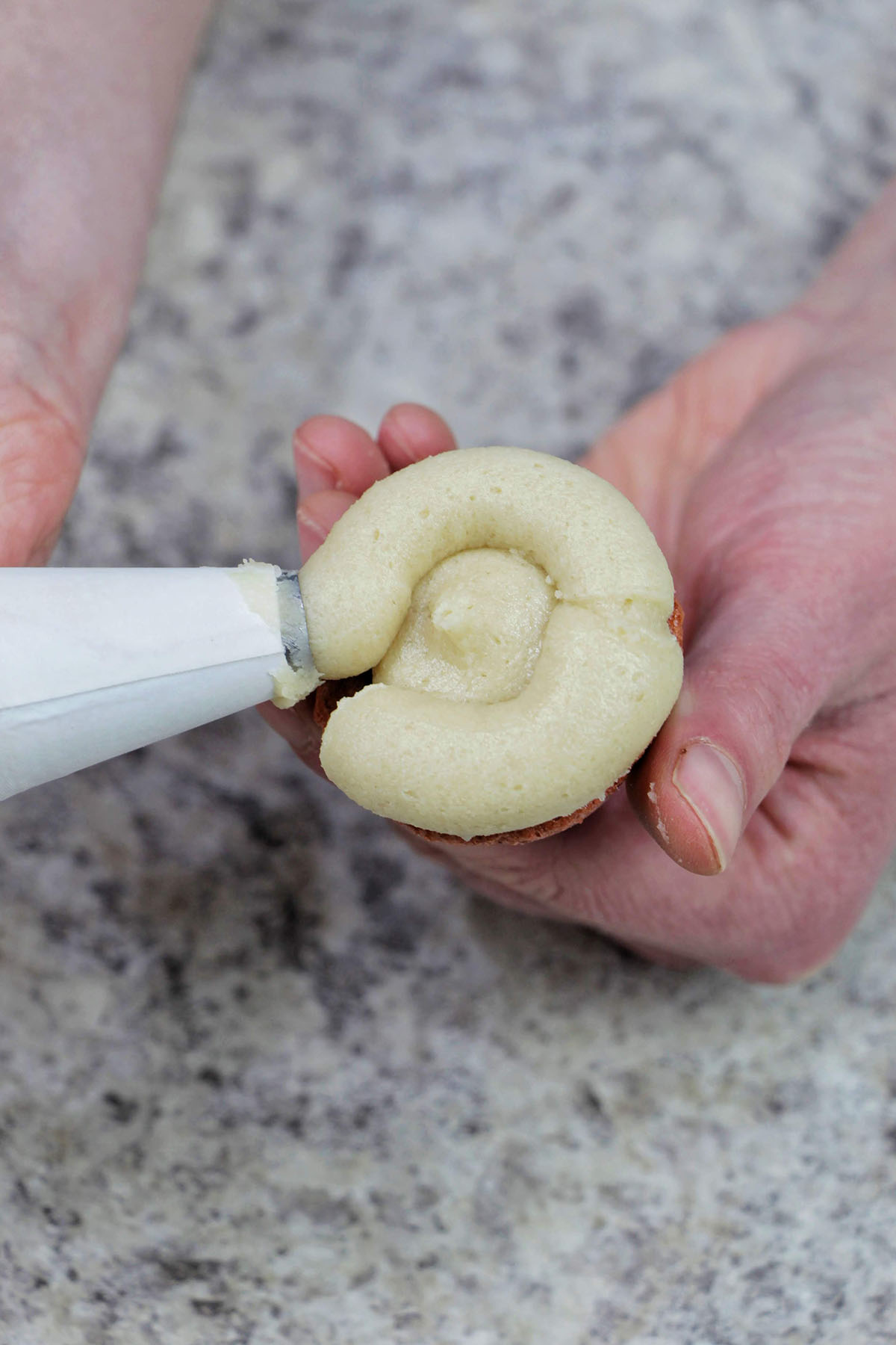 piping cookie dough buttercream onto a brown macaron.