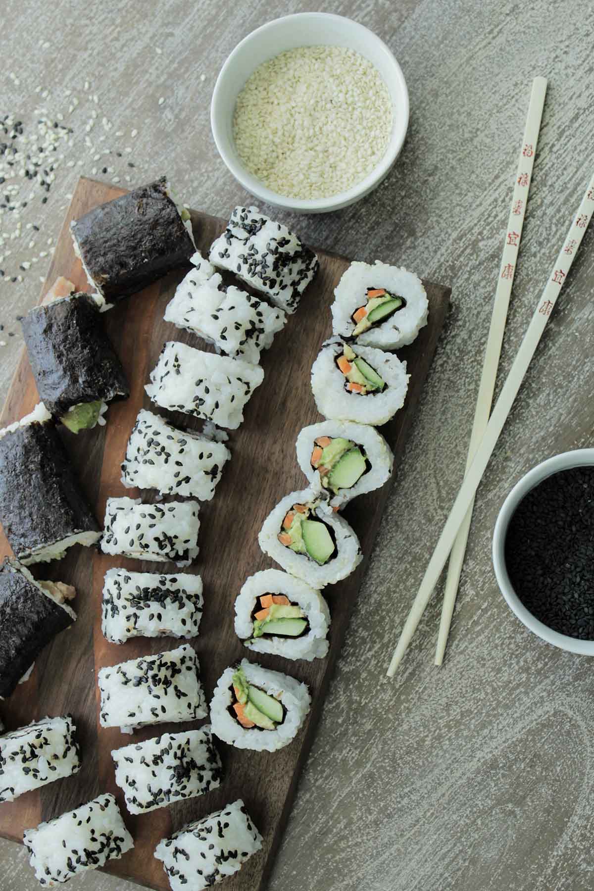 sushi rolls next to chopsticks and sesame seeds.