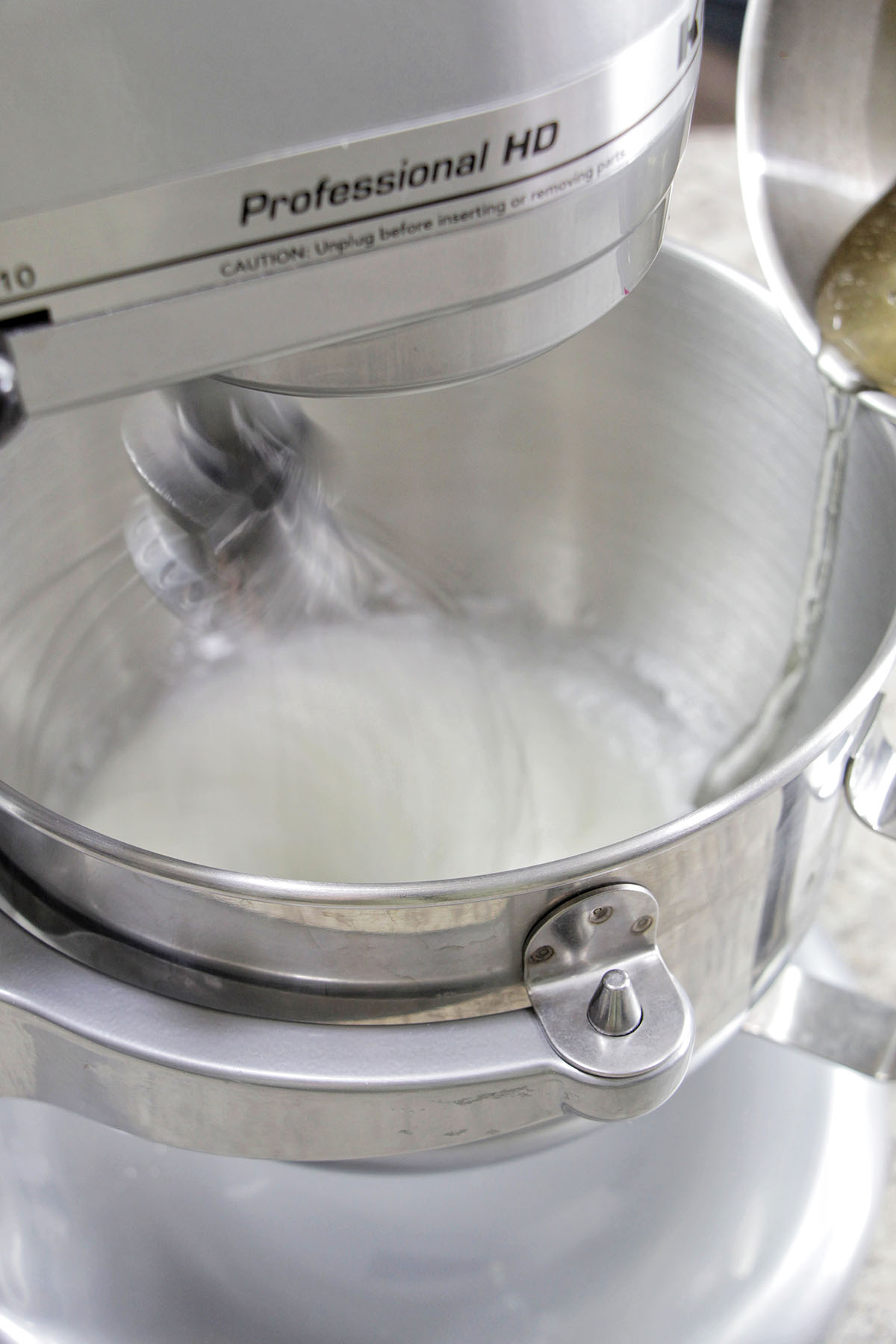 pouring hot sugar syrup into whipped egg whites in a stand mixer.