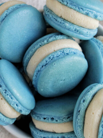 bowl filled with blue macarons filled with buttercream frosting.