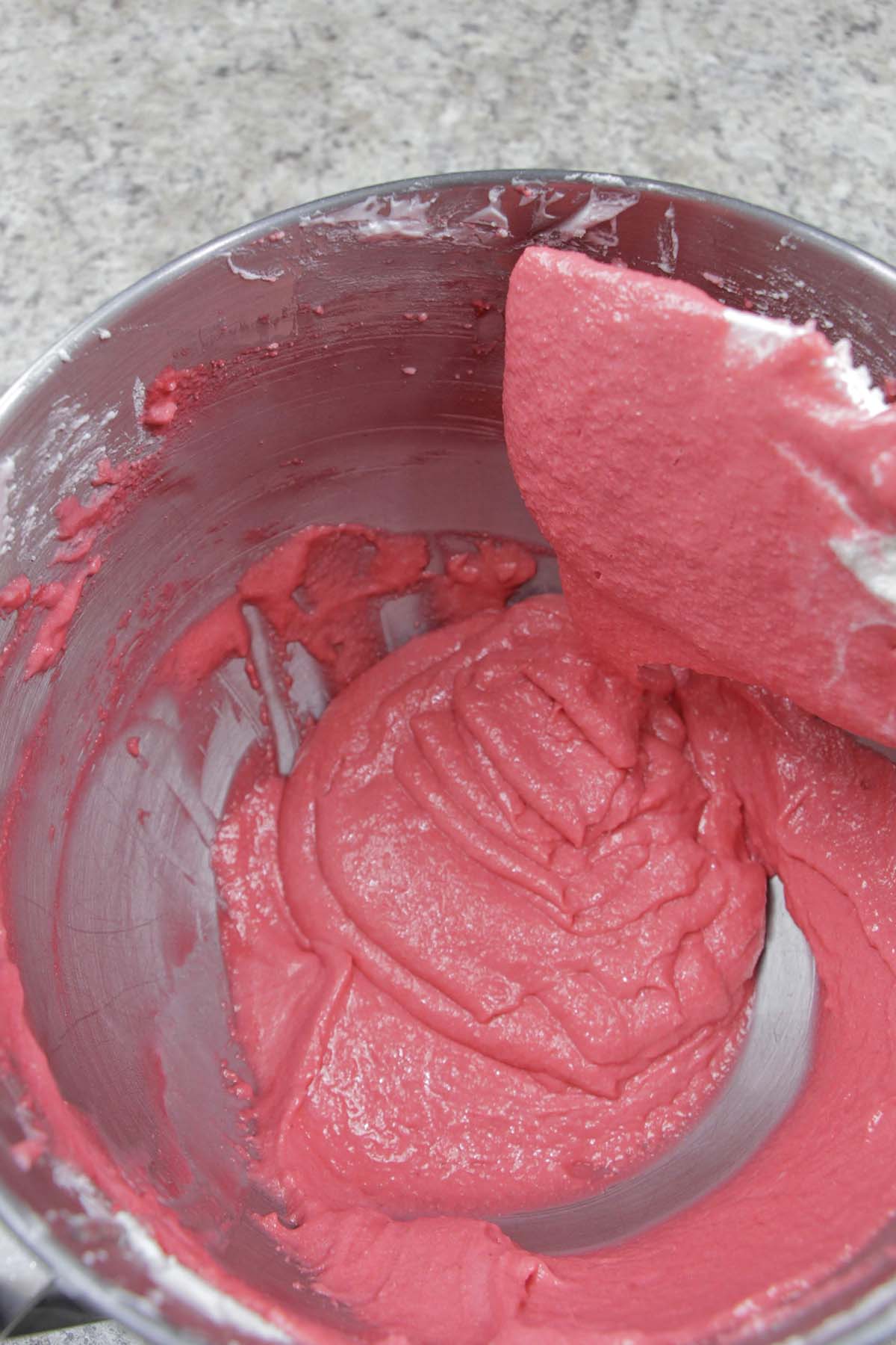 red macaron batter running of a silicone spatula.