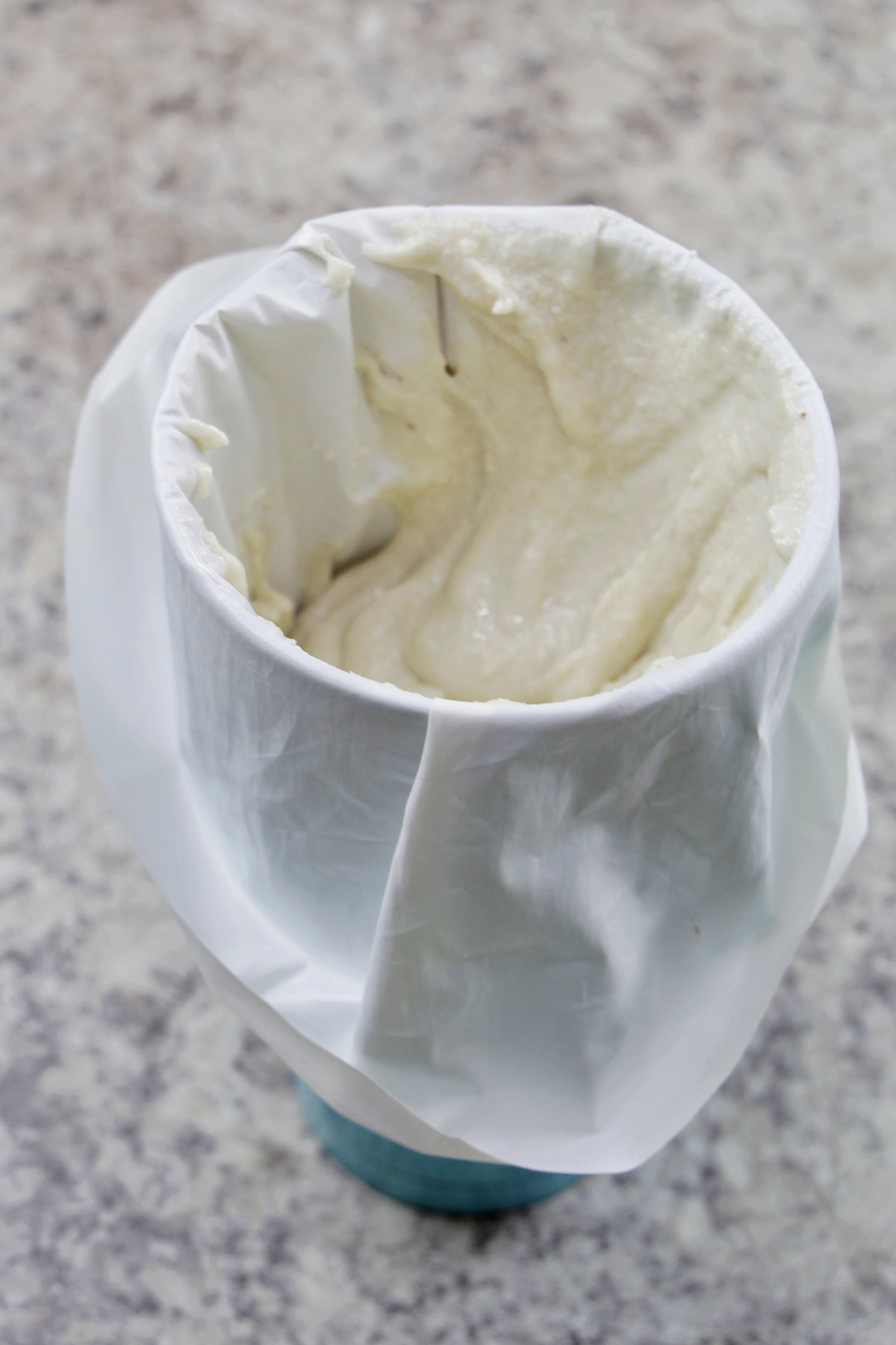 white macaron batter in a piping bag draped over a large cup.