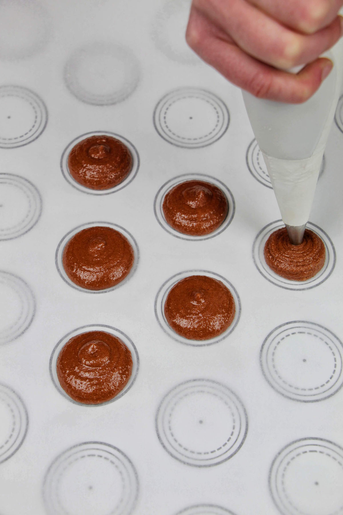 piping brown macaron batter onto a macaron template.