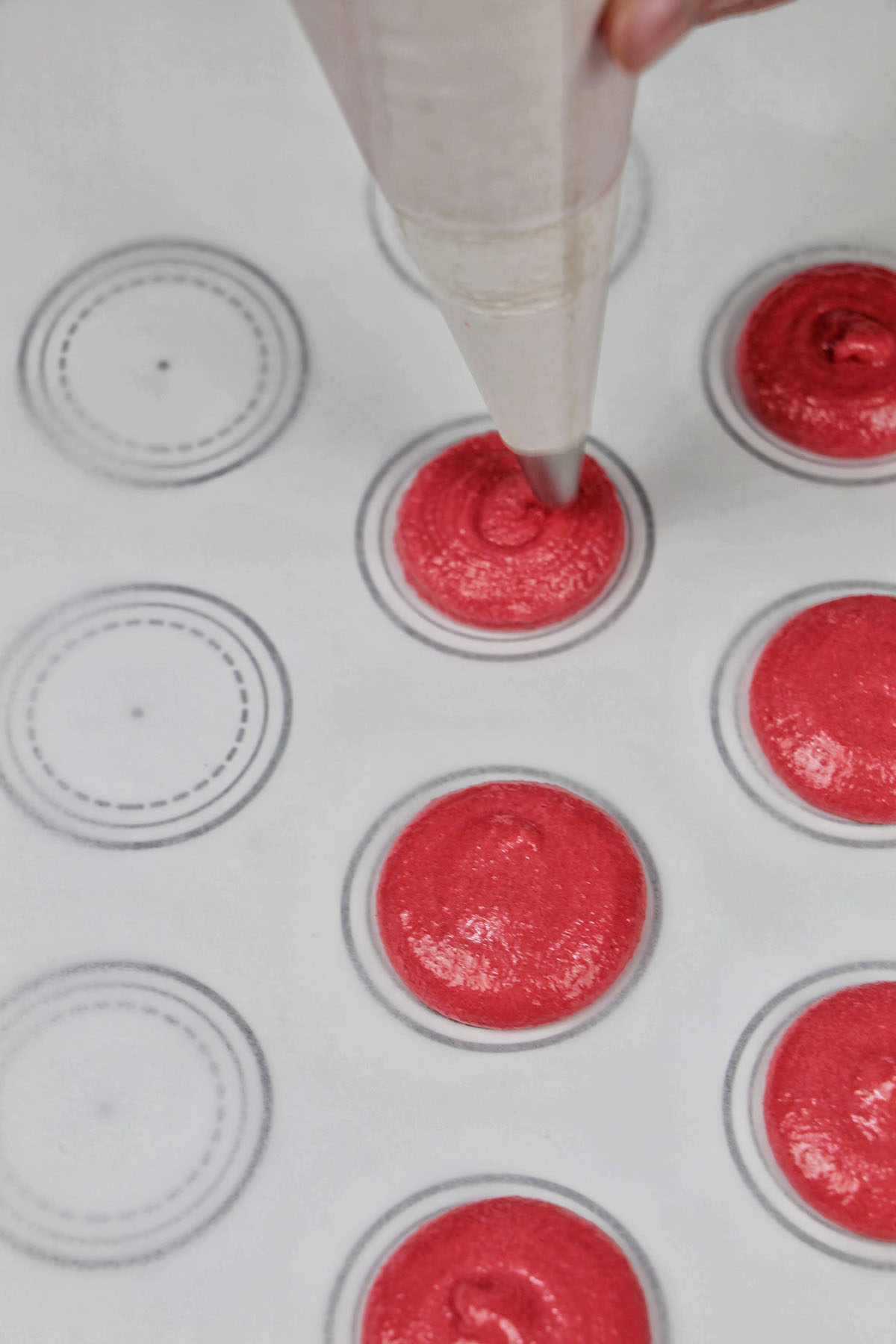 piping red macaron batter onto a macaron template.