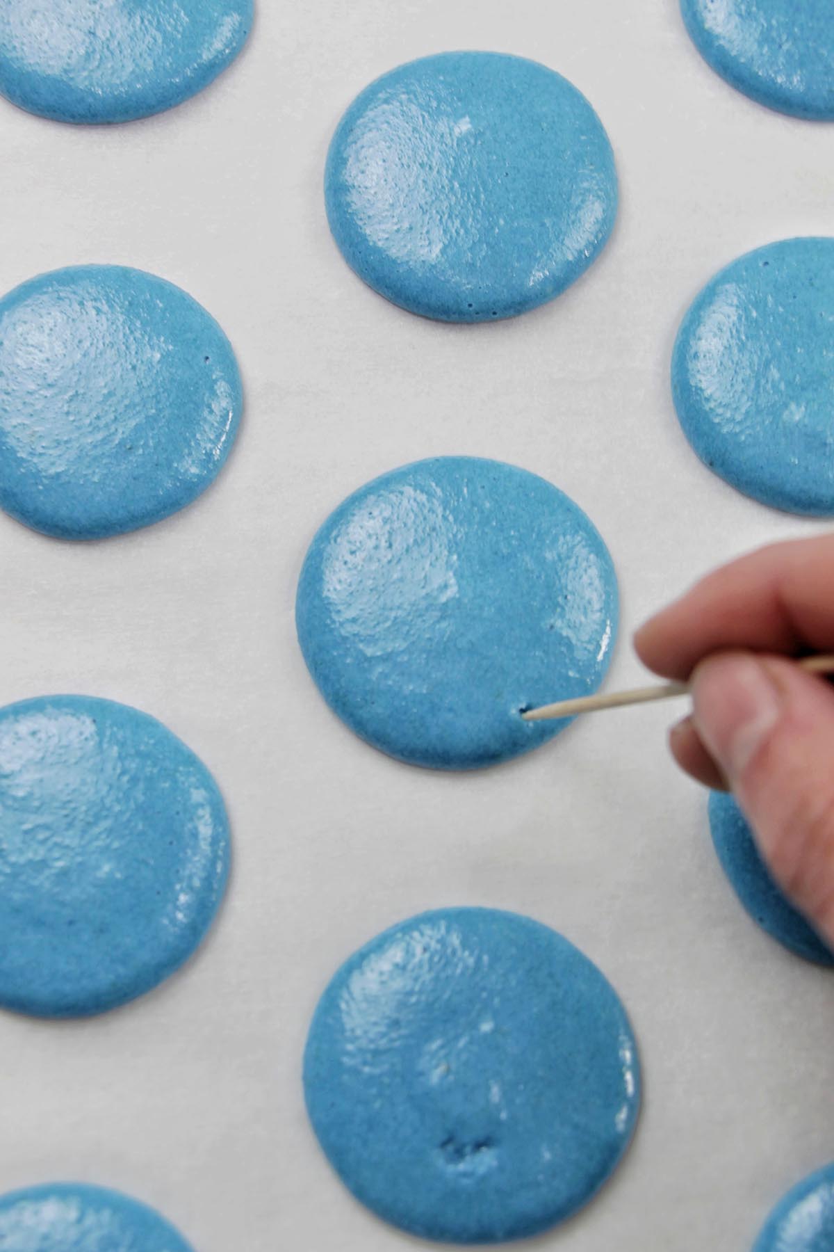 hand popping air bubbles on a macaron with a toothpick.