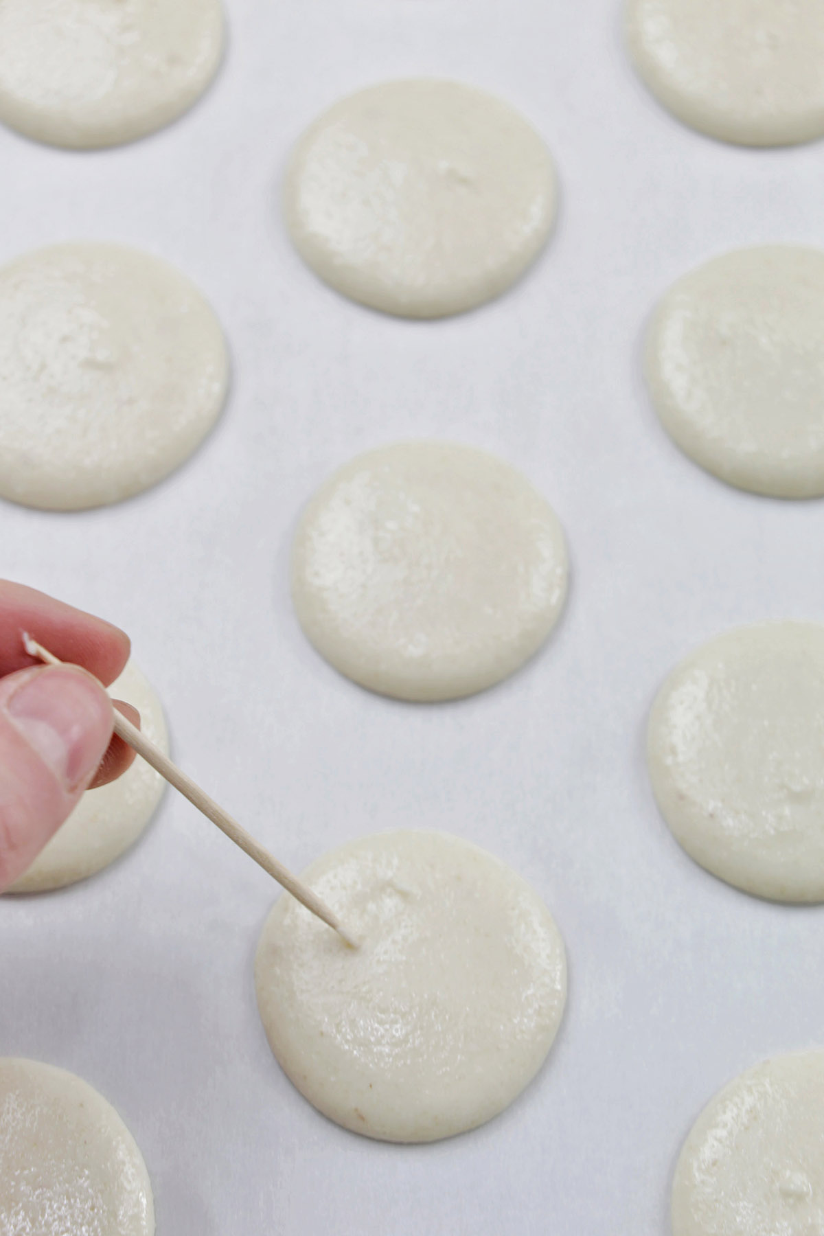 hand holding a toothpick popping air bubbles in macarons.