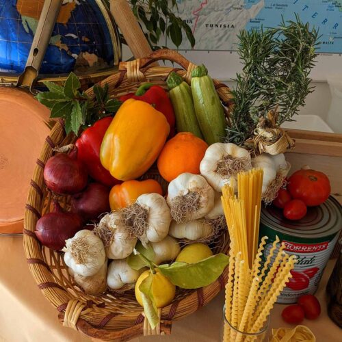 basket filled with various vegetables next to dried pasta and tomato sauce can.