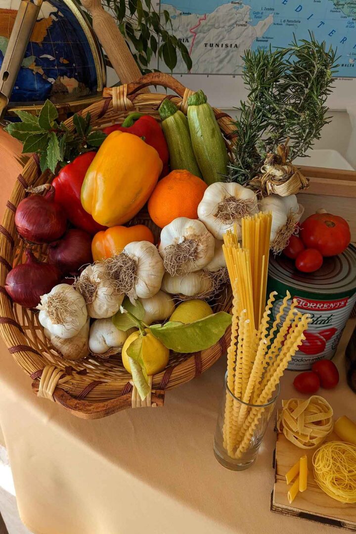 basket filled with various vegetables next to dried pasta and tomato sauce can.