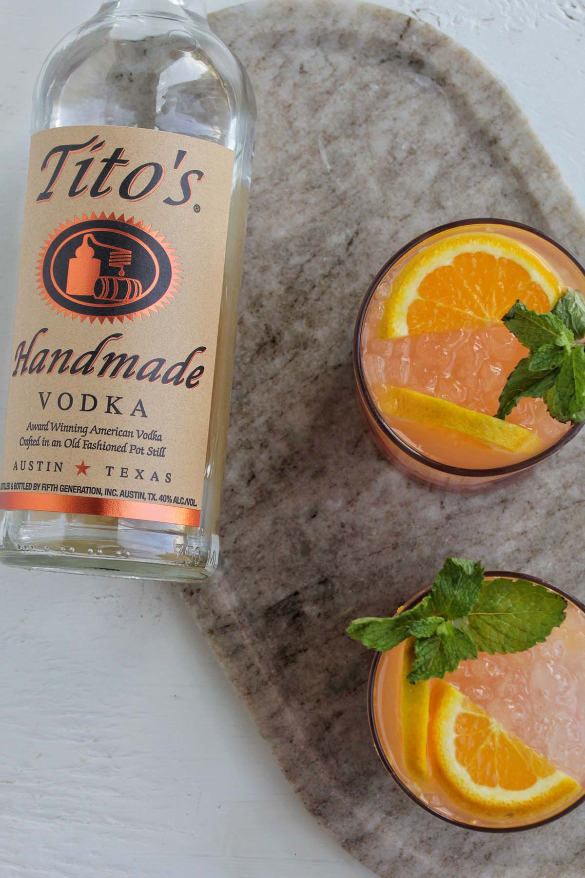 Tito's vodka bottle laying next to two orange cocktails.