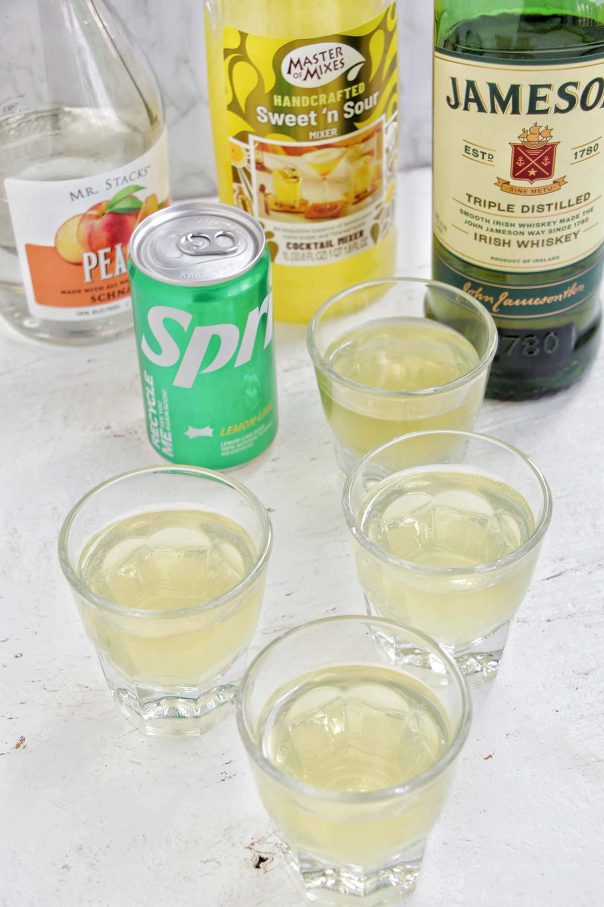 four green tea shots in rocks glasses next to alcohol bottles.